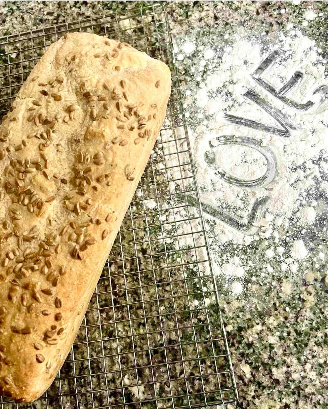 A seeded loaf on a cooling rack next to the word love written in flour